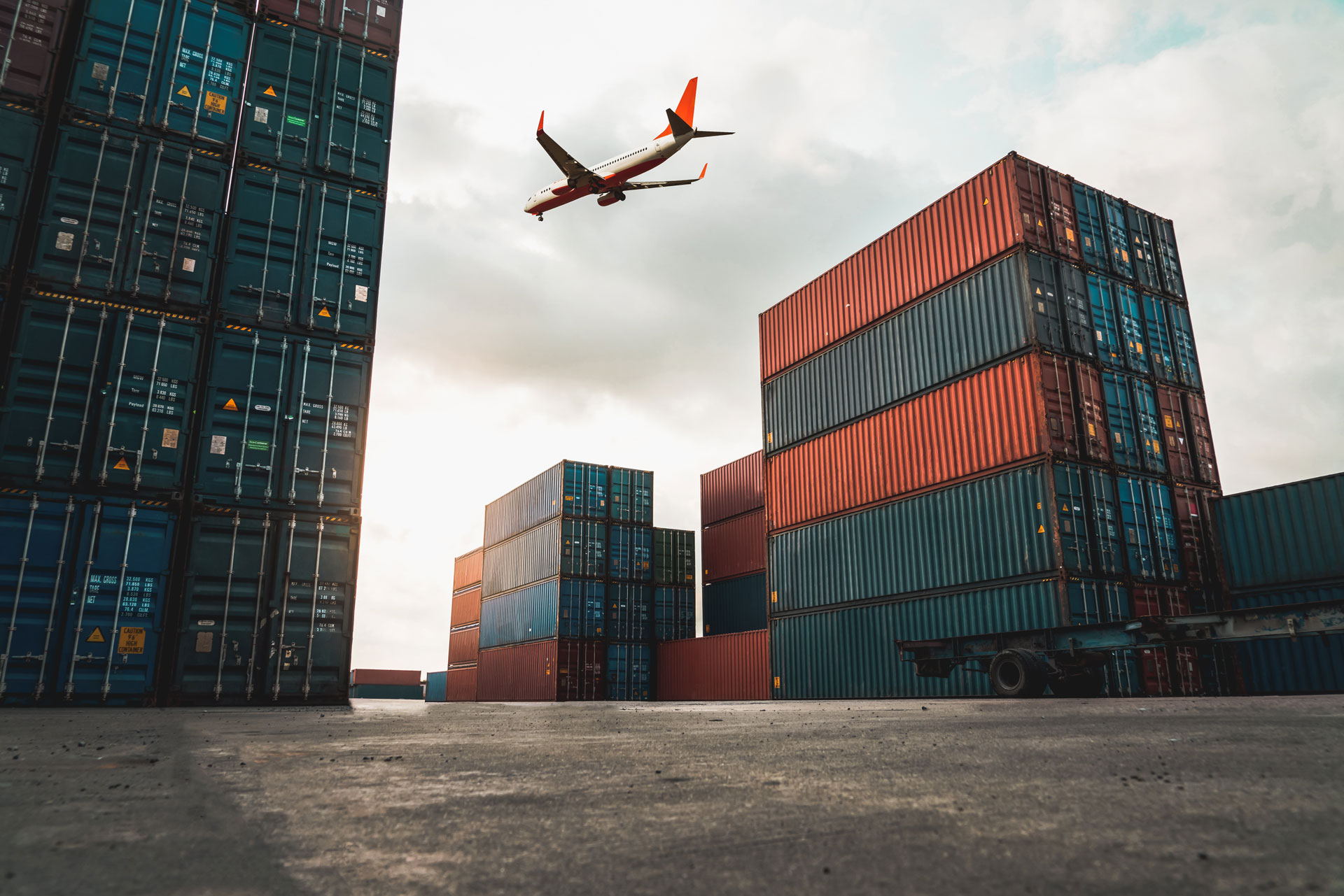 Freight airplane flying above overseas shipping container . Logistics supply chain management and international goods export concept .